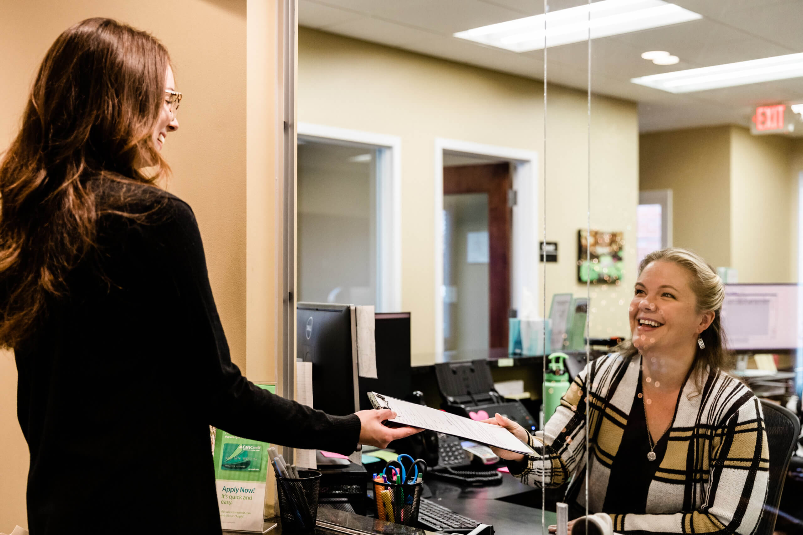 Garden Springs-47 Emily a receptionist and a patient smile while conversing and exchanging a clipboard with paperwork.